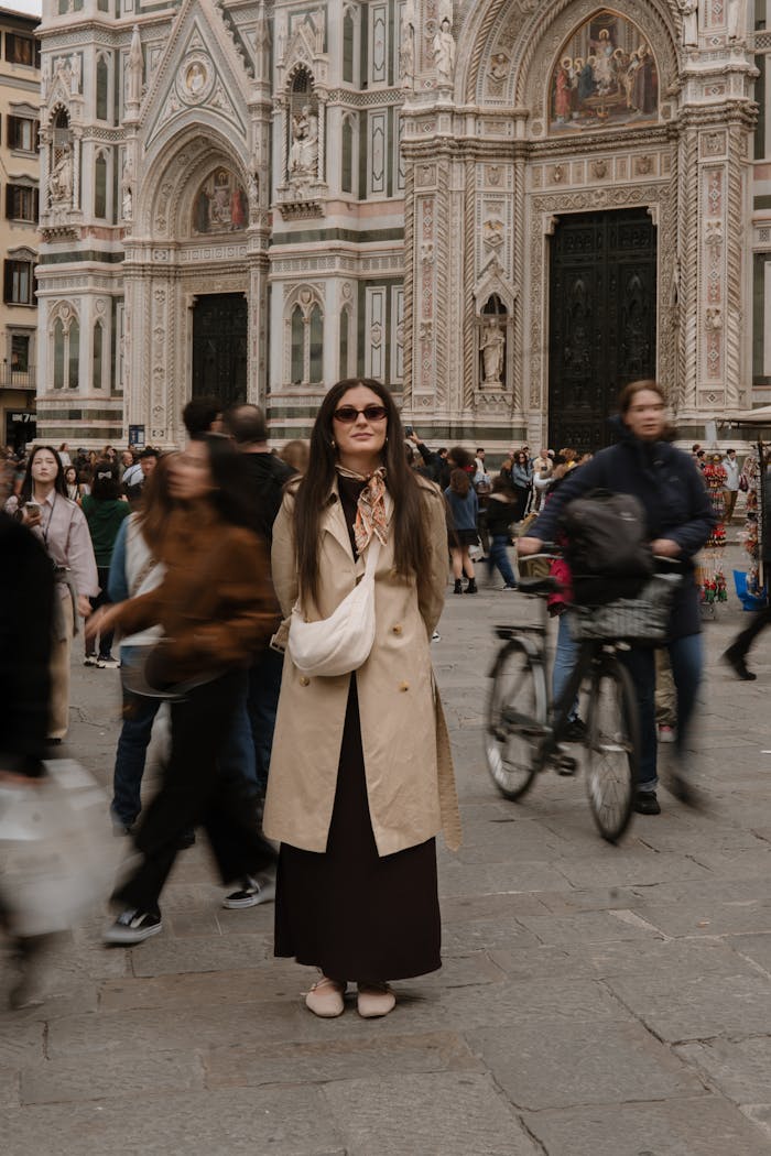 A stylish woman in sunglasses stands near Florence Cathedral, surrounded by motion blur of pedestrians and cyclists.