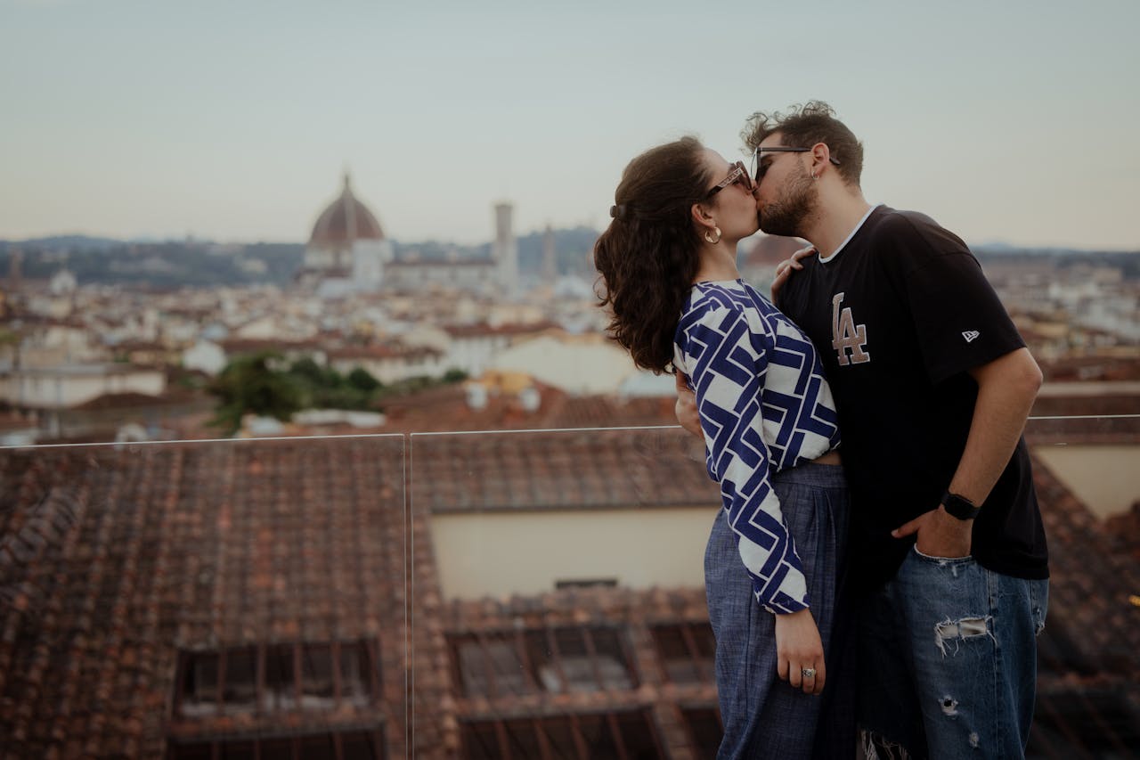 A couple shares a romantic kiss with the Florence skyline and iconic dome in the background.